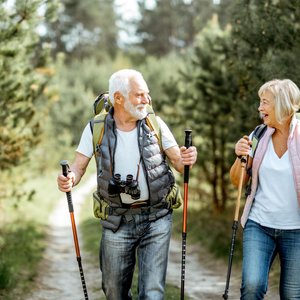 Ein älterer Mann und eine ältere Frau machen einen Spaziergang mit Walkingstöcken.