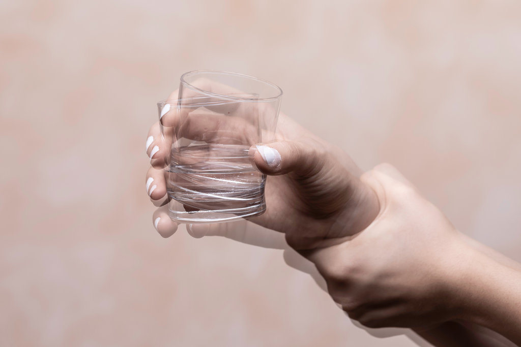 Eine zitternde Hand hält ein Glas Wasser.