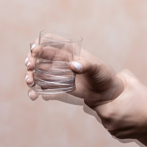 Eine zitternde Hand hält ein Glas Wasser.