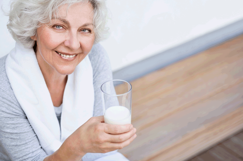 Eine Seniorin mit einem Glas Milch in der rechten Hand.