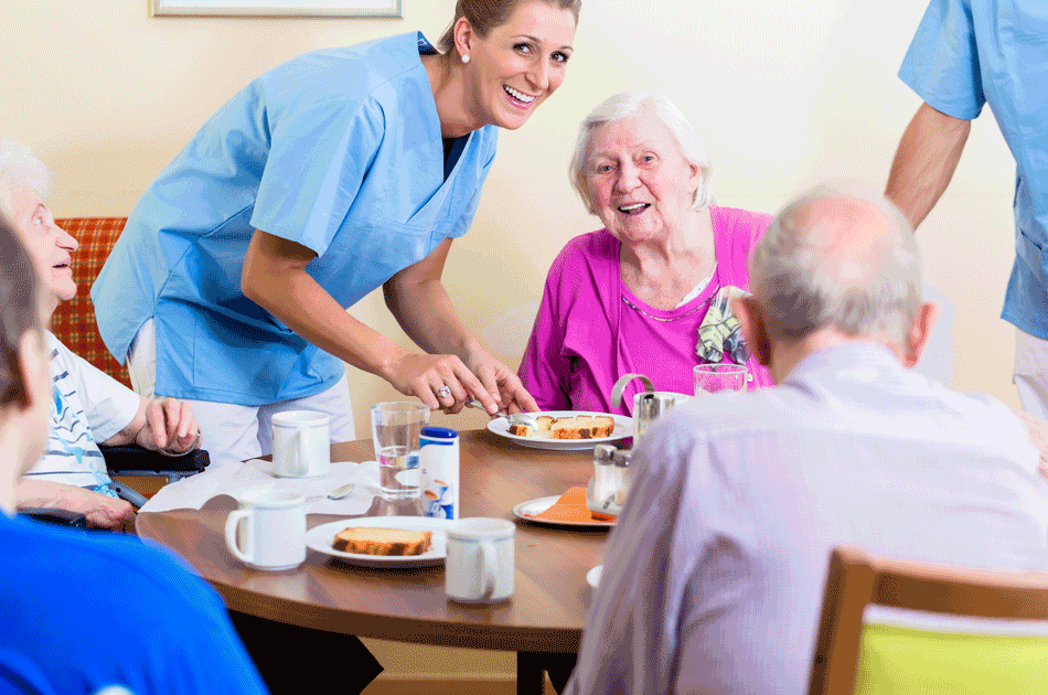 Eine Pflegerin bringt in einem Seniorenheim den Bewohnern Essen an den Tisch.