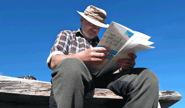 Ein Wanderer auf einer Bank mit Sonnemütze und Karte. 