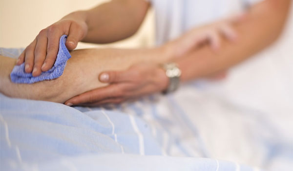 Eine osteuropäische Pflegekraft wäscht eine Frau die Hände, welche gerade im Bett liegt.