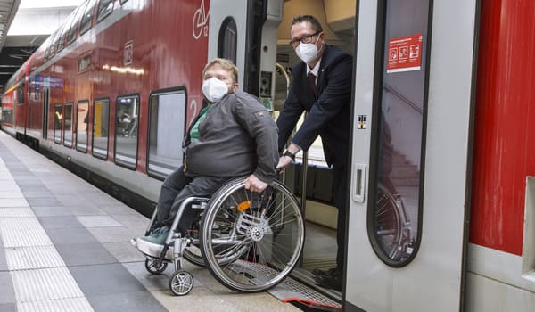Einem Rollstuhlfahrer wird am Bahnsteig geholfen in den Regionalzug zu kommen. 