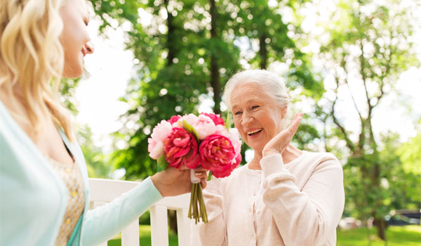 Eine junge Frau überreicht einer älteren Dame einen Blumenstrauß.