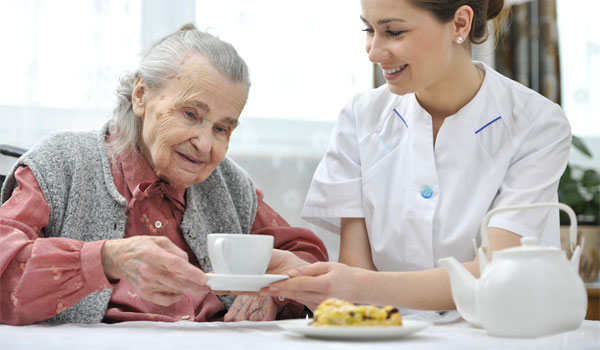 Eine Pflegerin reicht einer Seniorin im Pflegeheim eine Tasse Kaffee.