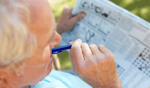 Ein älterer Herr sitzt vor einem Kreuzworträtsel und denkt nach. 