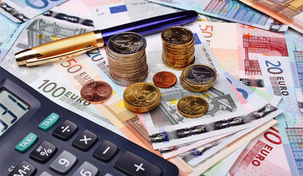 Ein Taschenrechner, ein Kugelschreiber und dazu Geldscheine und Münzen, verteilt auf einem Tisch. 