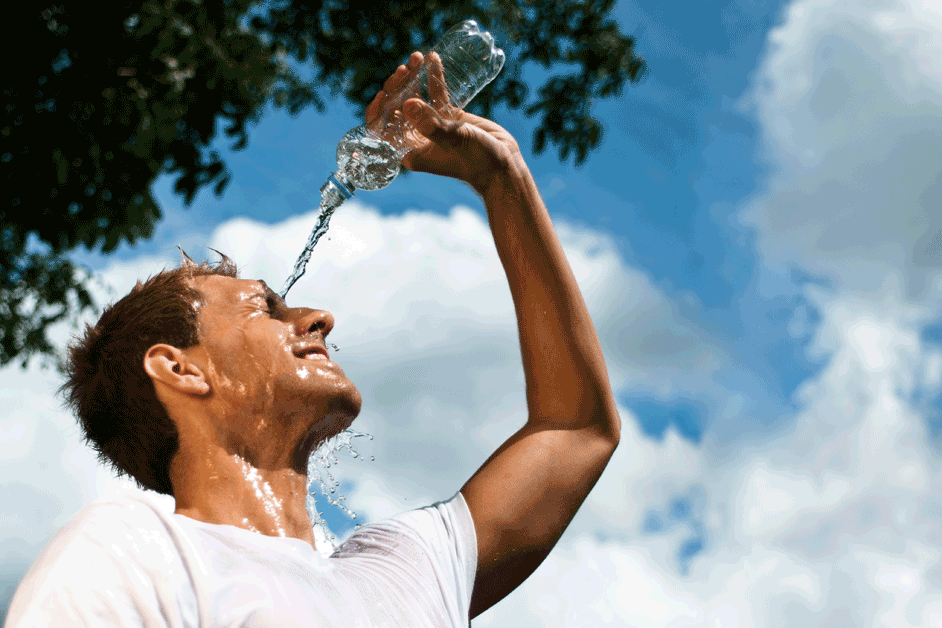 Ein Mann kühlt sich mit einer Flasche Wasser, die er sich über den Kopf gießt, ab.