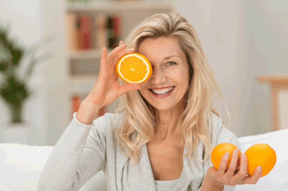 Eine Frau mit zwei Orangen in der Hand. Eine offene Ornage hält sie vor ihr Gesicht.
