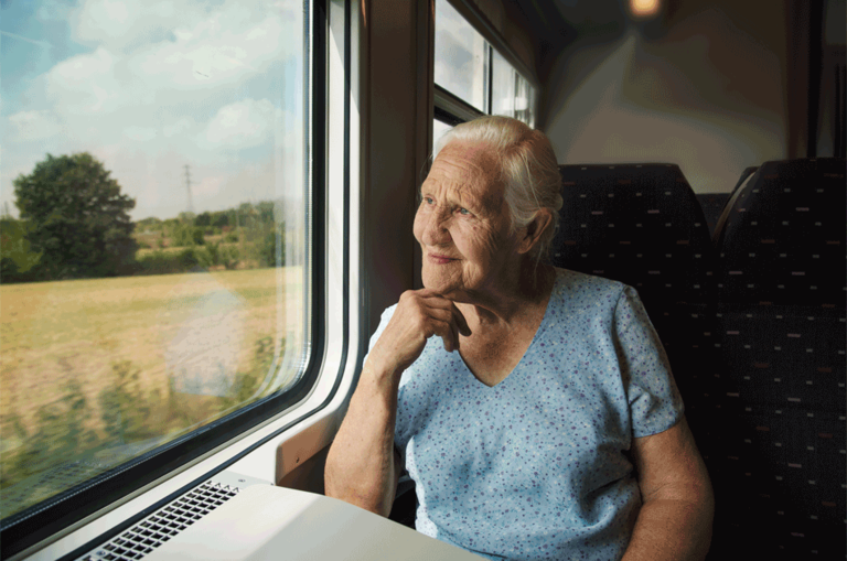 Eine ältere Dame sitzt im Zugabteil und schaut aus dem Fenster.