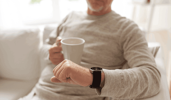 Ein Senior schaut im Wohnzimmer, auf seiner Couch sitzend, auf seine Limmex Notruf-Uhr.