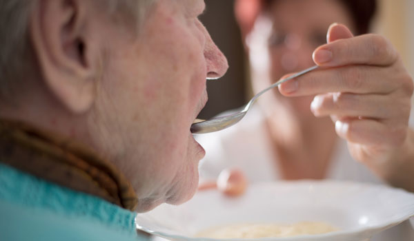 Eine Seniorin wird gefüttert und bekommt ein Löffel Suppe von einer Pflegerin.