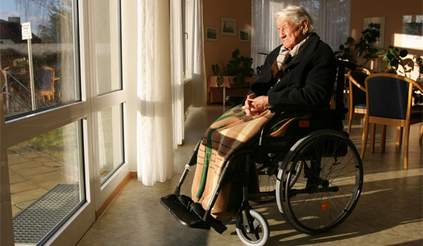 Mann sitzt im Rollstuhl und schaut aus dem Fenster des Seniorenheims.