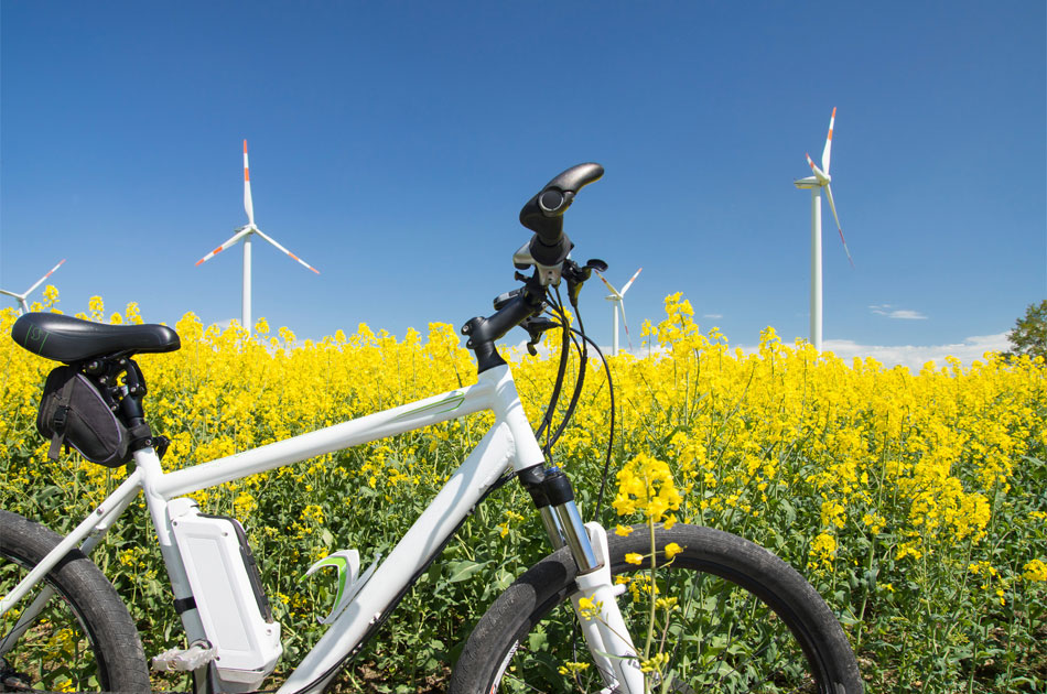 E-Bike in der Natur vor zwei Windkrafträdern.