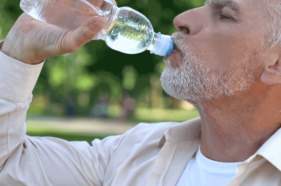 Ein Senior trinkt aus einer Flasche Wasser.