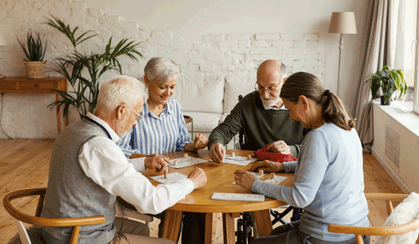 4 Senioren sitzen an einem runden Tisch und spielen Bingo.