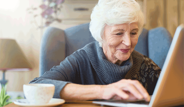 Eine Seniorin sitzt an ihrem Leptop.