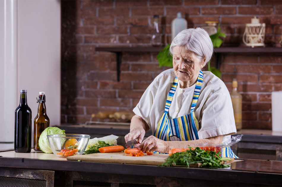 Seniorin mit Schürze in der Küche beim schneiden von Gemüse.