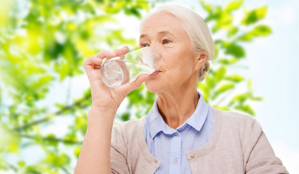 eine seniorin trinkt ein Glas Wasser.