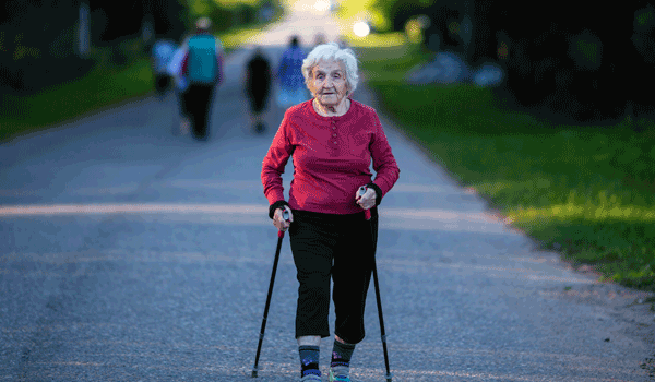 Eine Seniorin beim Nordic Walking im Park.