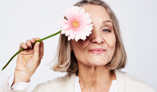 Eine Seniorin, die sich eine Blume vor dem rechten Auge hält.