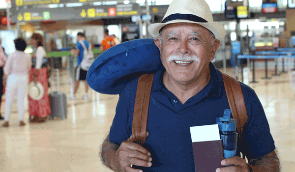Ein Senior am Flughafen mit seinen Papieren in den Händen und einen Rucksack auf der Schulter tragend.