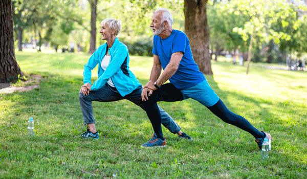 Ein älteres Ehepaar wärmt sich vor dem Sport mit Dehnübungen in einem Park auf.