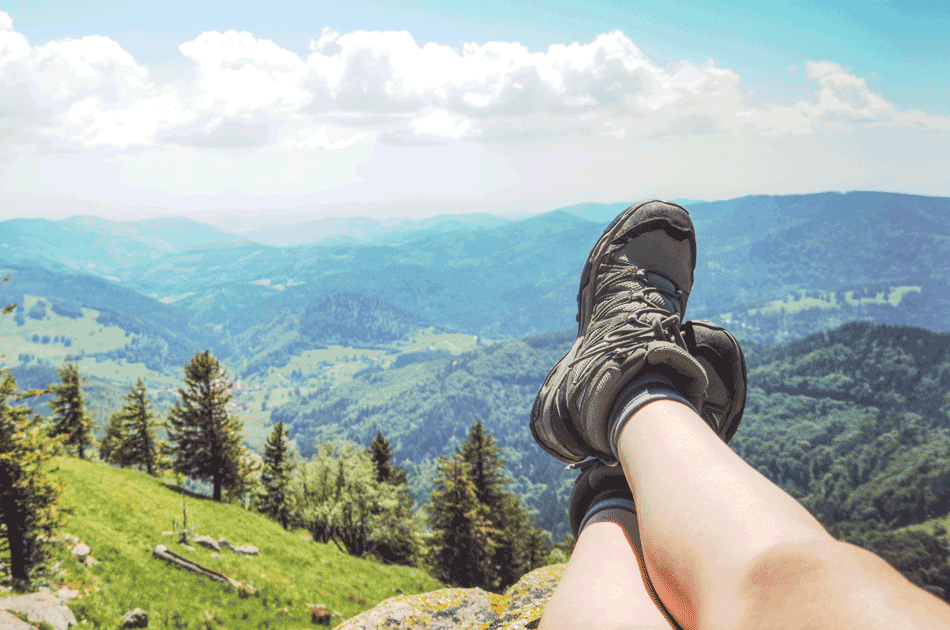 Eine Frau genießt nach einer Wanderung das Bergpanorama. Zu sehen sind nur die Beine.