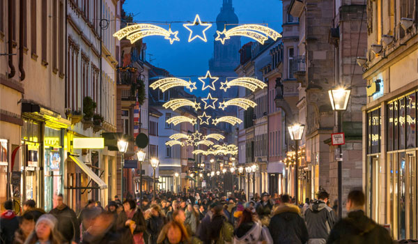 beleuchtete Straße in einer Innenstadt zur Weihnachtszeit, wo viele Menschen unterwegs sind.