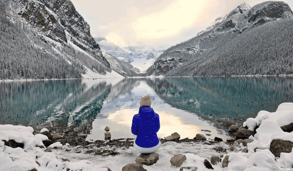 Ein eFRau sitzt an einem See und genießt den Ausblick auf das Wasser und schneebedeckten Berge.
