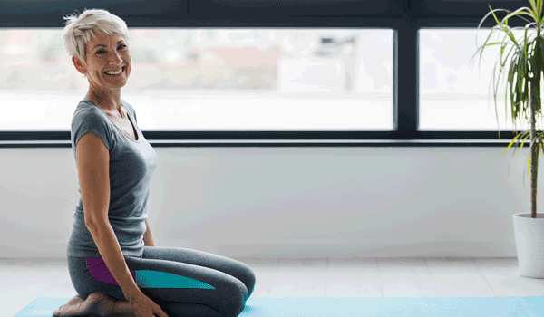Eine Frau sitzt auf einer Yogamatte und startet mit Ihrem täglichen Yoga Übungen.