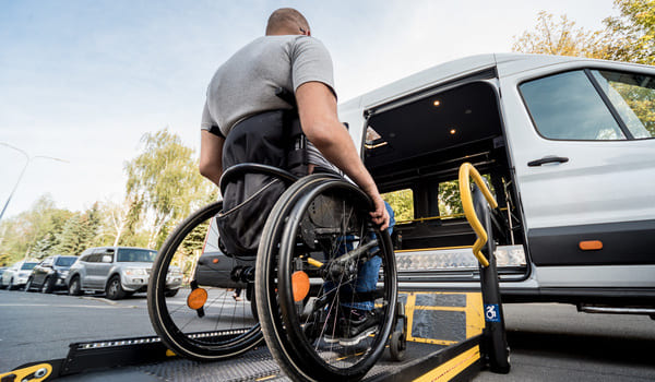 Ein Rollstuhlfahrer besteigt mit einer transportablen Hebebühne ein Transportauto.