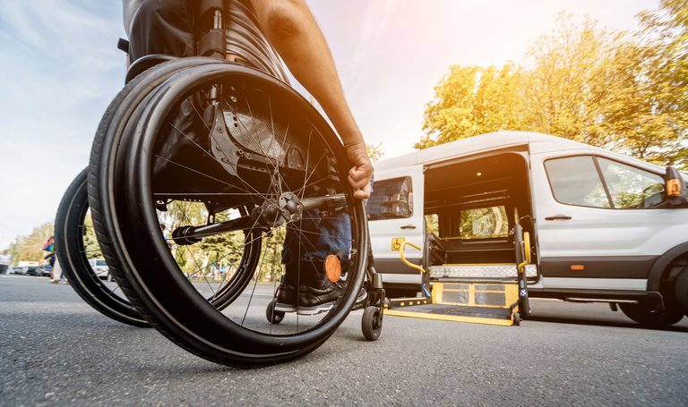 Ein Rollstuhlfahrer besteigt mit einer transportablen Hebebühne ein Transportauto.
