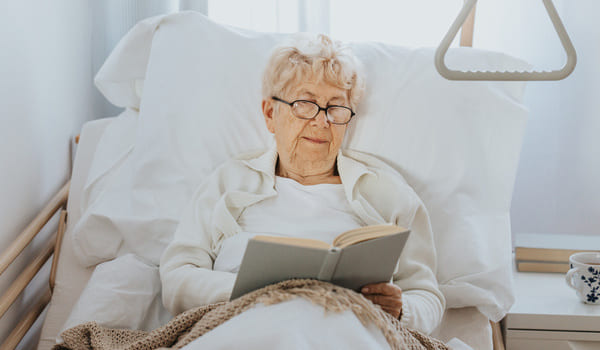 Eine Seniorin liegt in ihrem Pflegebett und liest.