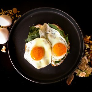 Zwei Spiegeleier auf Spinat und Brot auf einem schwarzen Teller