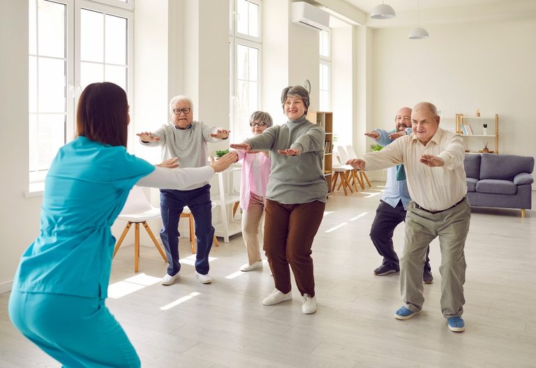 Eine Physiotherapeutin zeigt einer Seniorengruppe eine Gymnastikübung.