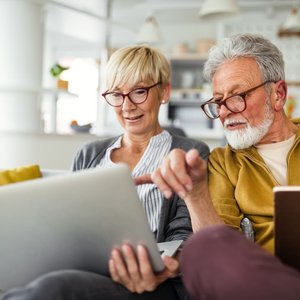 Eine ältere Frau und ein Mann sitzen vor ihren Laptops.